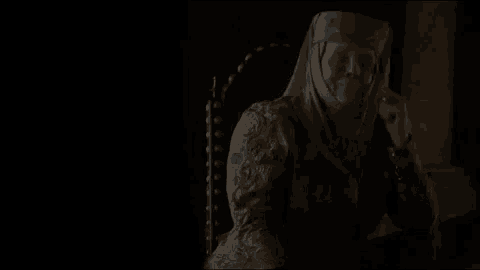a woman in a medieval dress is sitting in a chair in a dark room talking on a cell phone .