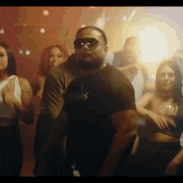 a man wearing sunglasses is dancing in front of a crowd of women .