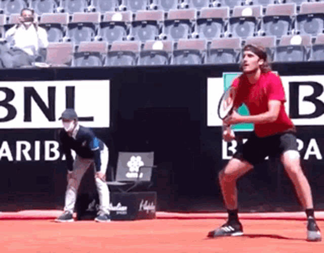 a man in a red shirt is holding a tennis racquet in front of a bnl sign