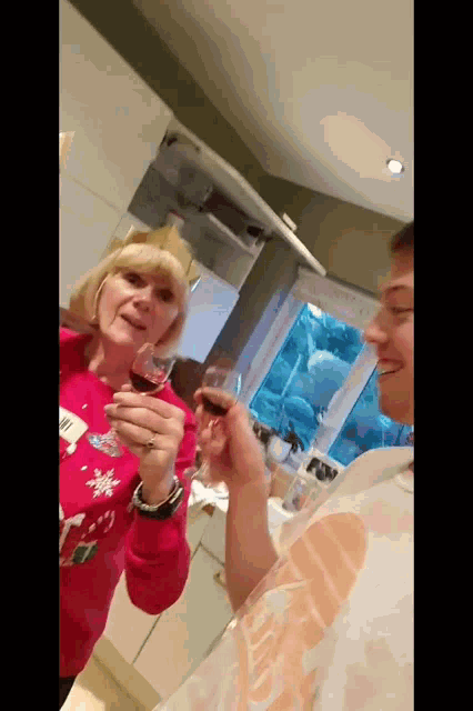 a woman in a red sweater holds a glass of wine in front of a man