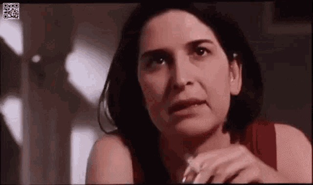 a woman in a red tank top is holding a cigarette in her hand and looking at the camera .