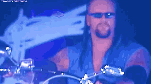a man with long hair and sunglasses is riding a motorcycle in a dark room .
