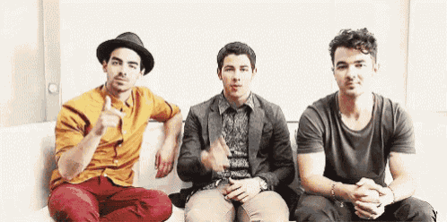a group of three men are sitting on a couch and one of them is wearing a hat .
