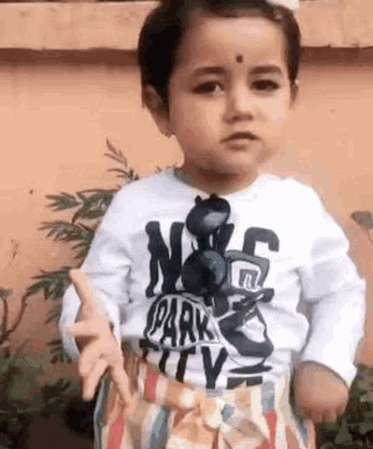 a little girl is wearing a white shirt and striped skirt and making a funny face .