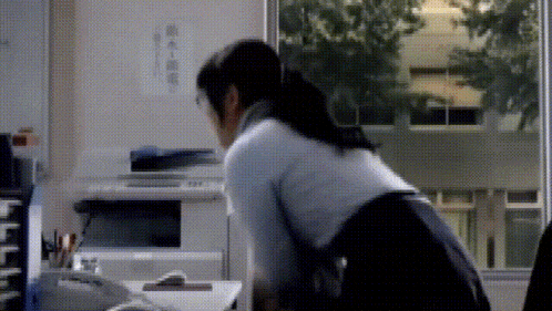 a woman is sitting at a desk in front of a window with chinese writing on it