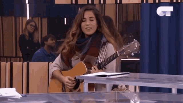 a woman playing a guitar in front of a blue curtain with the letter c on it