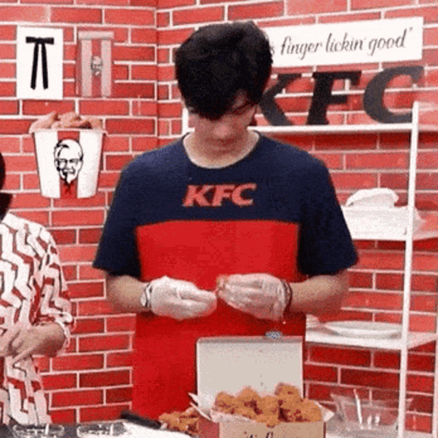 a man wearing a kfc shirt is opening a box of chicken nuggets