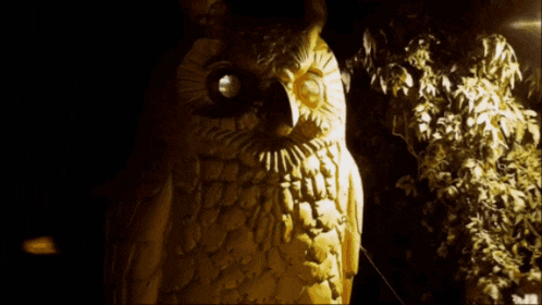a statue of an owl is lit up at night with a tree in the background