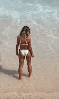 a woman in a white bikini is standing on a beach looking at the water .