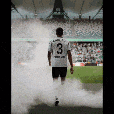 a soccer player with kapuadi on the back of his shirt walks on the field