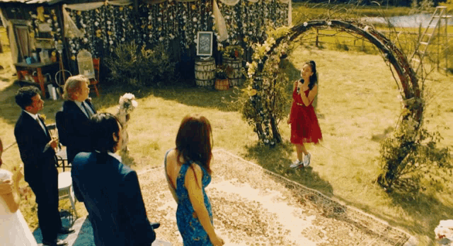 a woman in a red dress is singing into a microphone in front of a floral arch