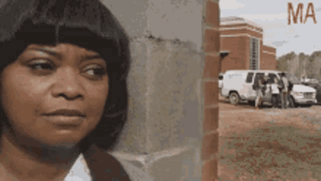 a woman is leaning against a brick wall and the word ma is on the bottom right