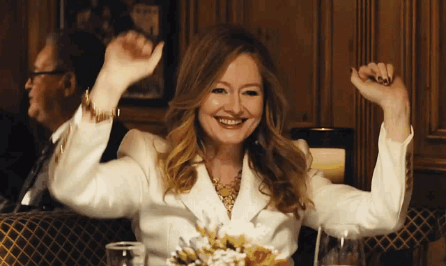 a woman in a white jacket is smiling and raising her arms in the air