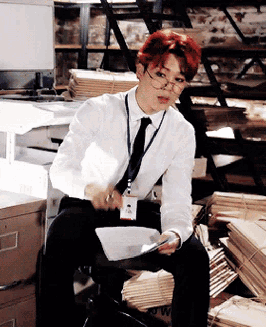 a man in a white shirt and tie is sitting in front of a stack of cardboard boxes