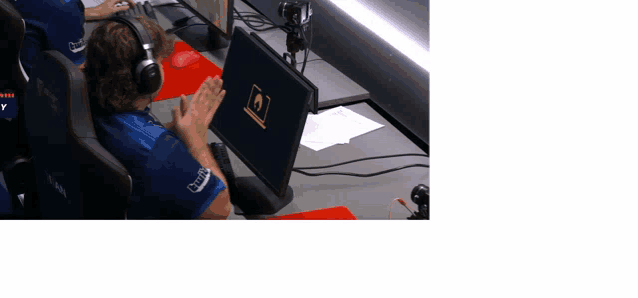 a man wearing headphones applauds in front of a computer screen that says ' corsair ' on it