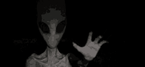 a black and white photo of an alien with glowing eyes and a hand in the dark .