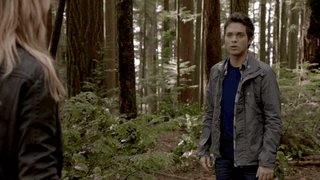 a man and a woman are standing in the woods and the man is wearing a grey jacket