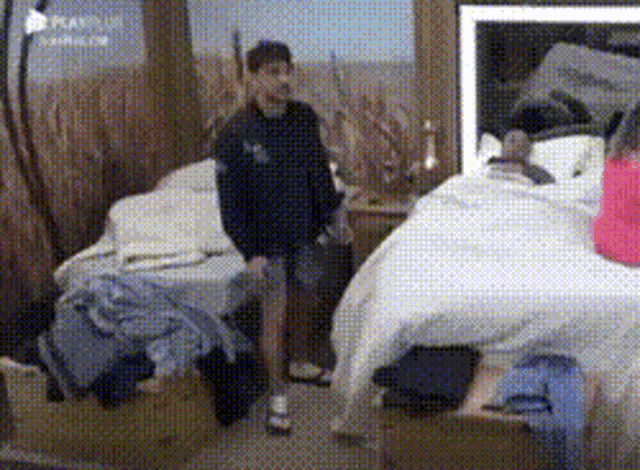 a man in a black jacket is standing in a bedroom next to two beds .
