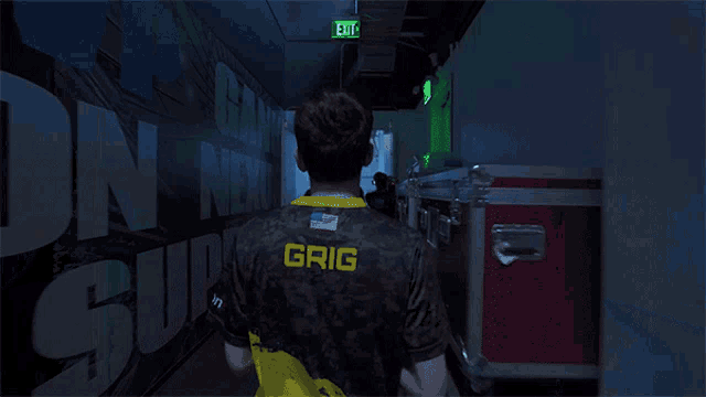 a man wearing a hyperx shirt walks down a dark hallway