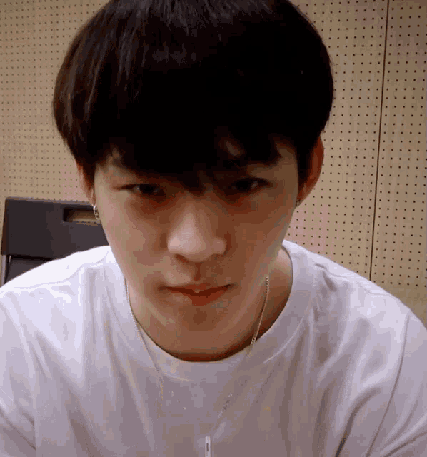 a young man wearing a white t-shirt and a necklace with the letter t on it