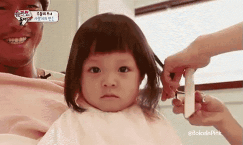 a baby girl is getting her hair cut by a man .