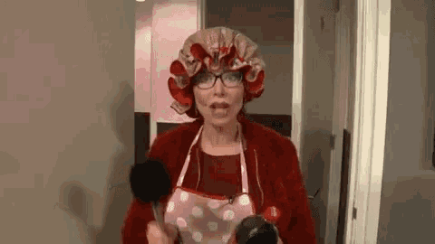 an elderly woman wearing a hat and apron is holding a spoon .