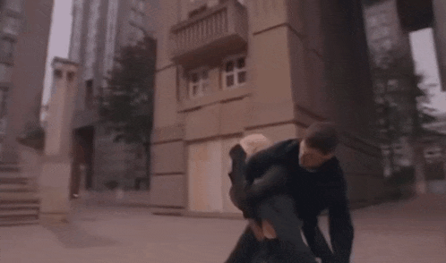 a man is carrying another man in his arms in front of a building .