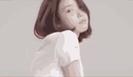 a woman wearing a white t-shirt with a camera on the sleeve is looking at the camera .