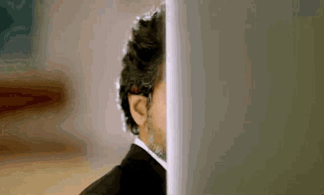 a man in a suit is peeking out from behind a computer screen