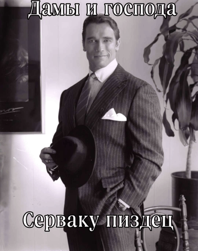 arnold schwarzenegger in a suit and tie holding a hat with a caption in a foreign language