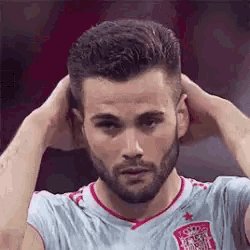 a man with a beard is holding his hair in his hands while wearing a soccer jersey .