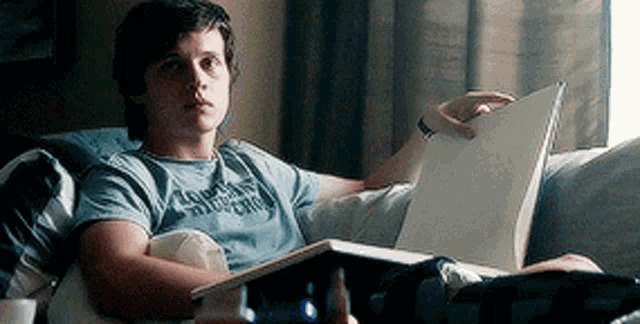 a young man is reading a book while laying on a couch .