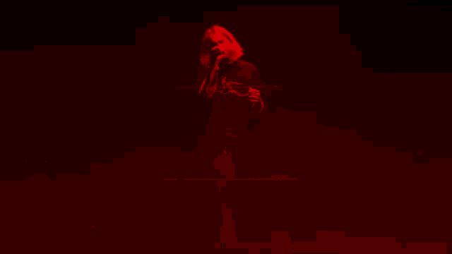 a woman with red hair is dancing in a dark room with red lights .