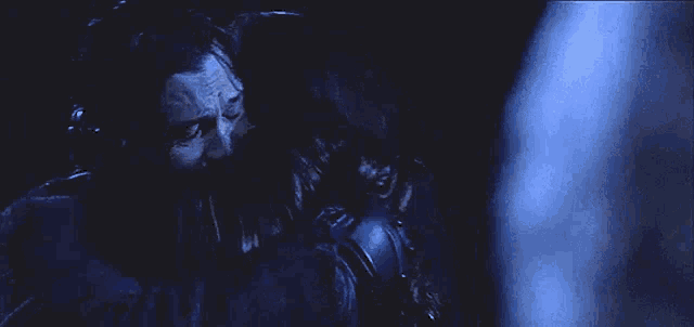 a man with a beard is sitting in a dark room holding a sword .