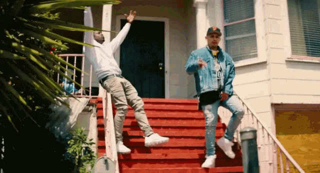 two men are standing on red stairs in front of a white house