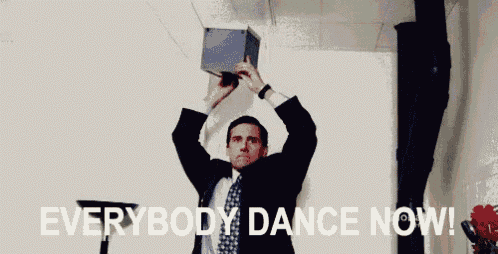 a man in a suit and tie is holding a box over his head with the words `` everybody dance now '' written below him .
