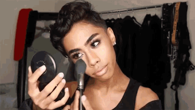 a young man is applying makeup to his face and looking at himself in a mirror .