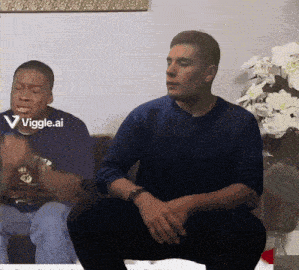 a man in a blue sweater is sitting next to another man in a blue shirt with the words viggle.ai on the bottom right