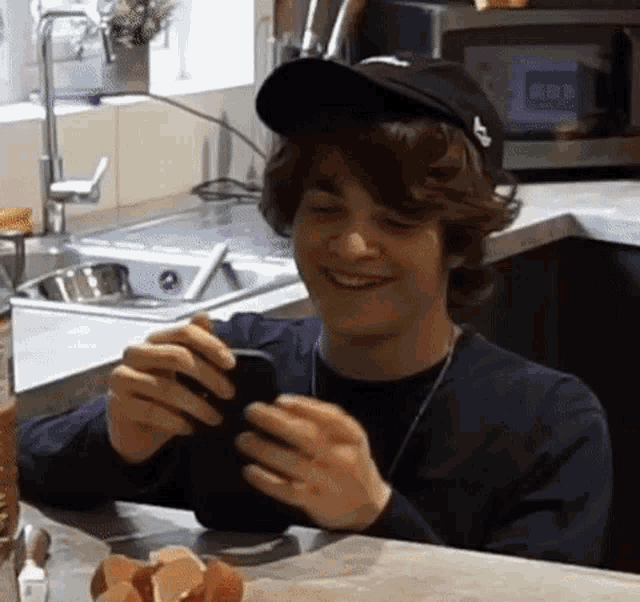 a young man wearing a baseball cap is smiling while looking at his phone