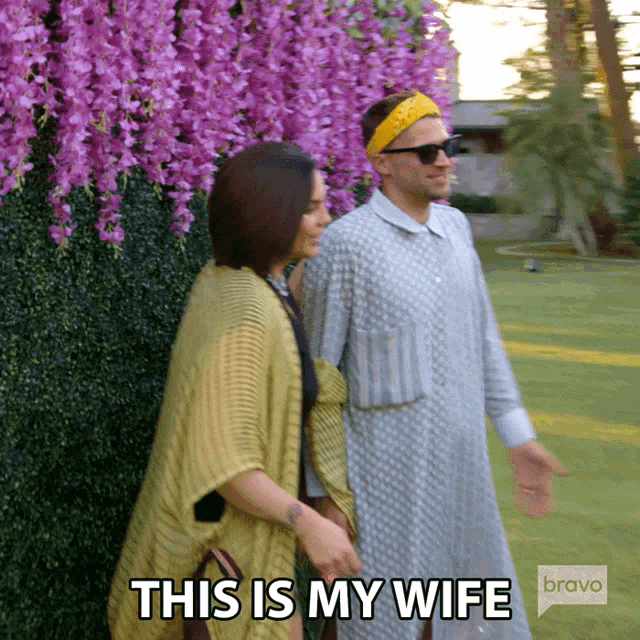 a man and woman are walking in front of purple flowers and the caption says this is my wife bravo