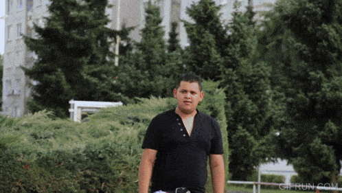 a man in a black shirt is standing in a park with trees in the background and the website gifrun.com in the corner