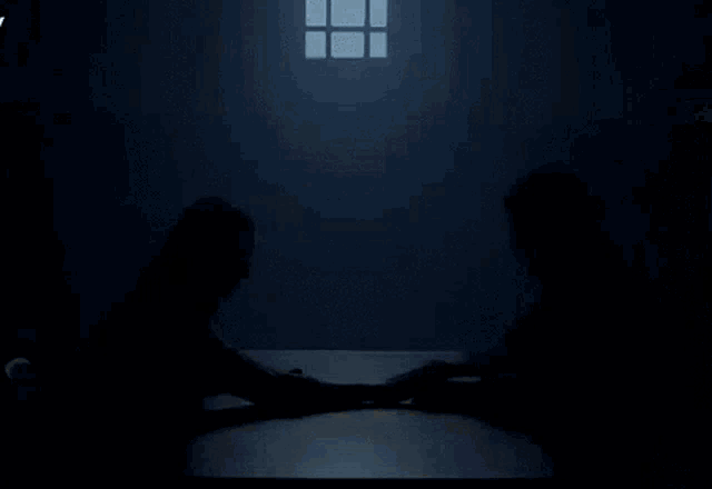 a man and woman are sitting at a table holding hands in a dark room .