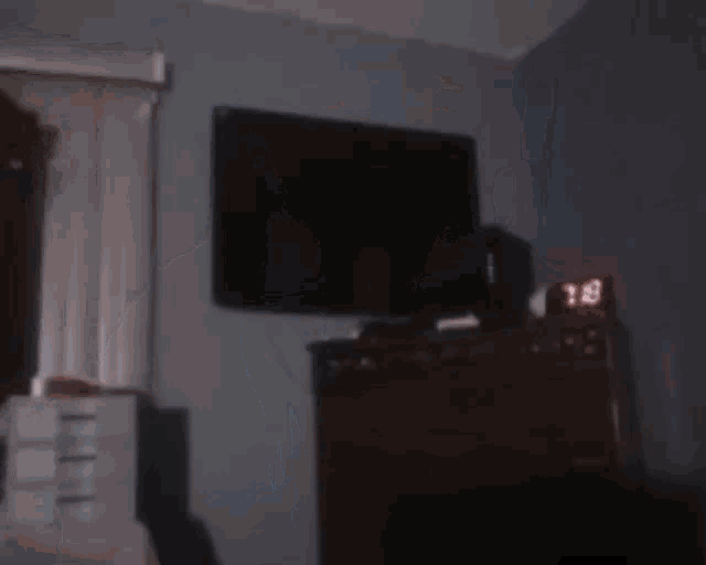 a blurred image of a person holding a remote control in a living room with a clock that says 10:13 .
