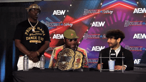 a man wearing a prince nan dance club shirt stands in front of a wall with aew written on it