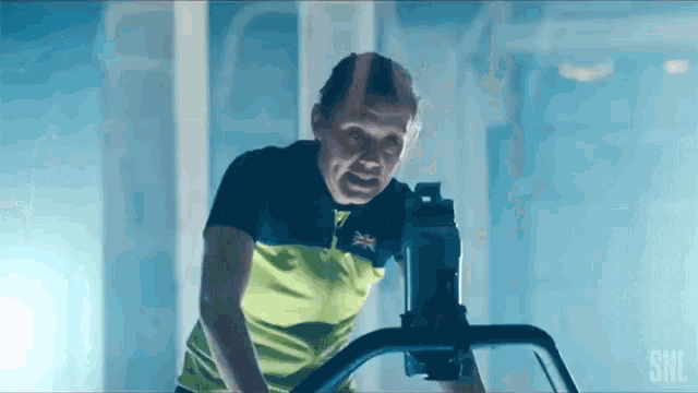 a man wearing a yellow shirt with the british flag on it rides an exercise bike
