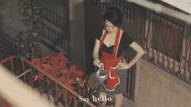a woman in a red apron is watering flowers on a balcony with a watering can .