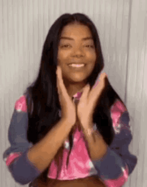 a woman in a pink and blue tie dye sweater is smiling and clapping her hands .
