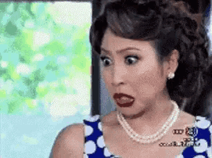 a woman wearing a blue and white polka dot dress and pearls is making a funny face .