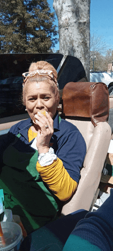 a woman in a green apron is sitting in a car eating a sandwich