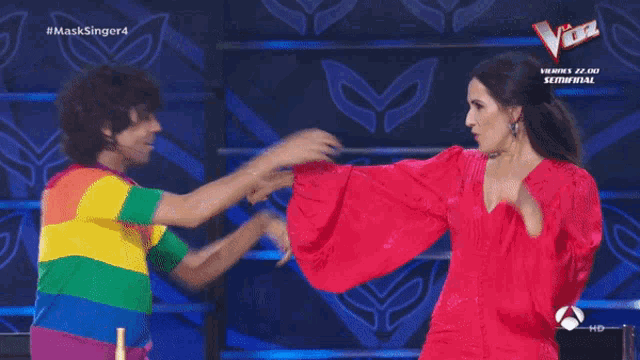 a woman in a pink dress and a man in a rainbow shirt are dancing on a stage